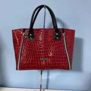Red crocodile-pattern handbag on display stand.