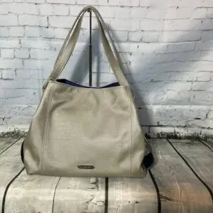 Beige handbag against white brick wall.